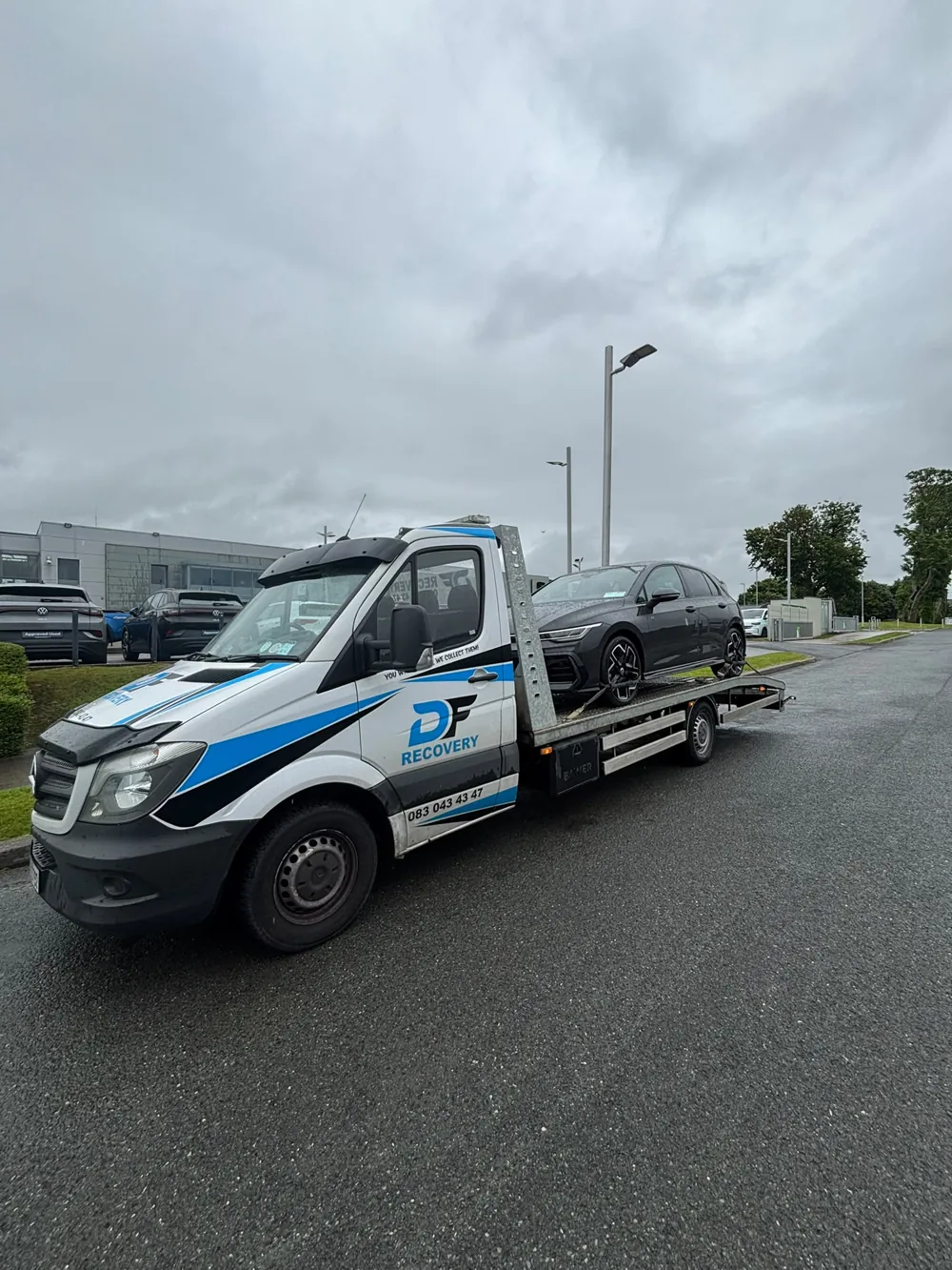 DF Recovery Mercedes flatbed carrying a grey Volkswagen outside a dealership